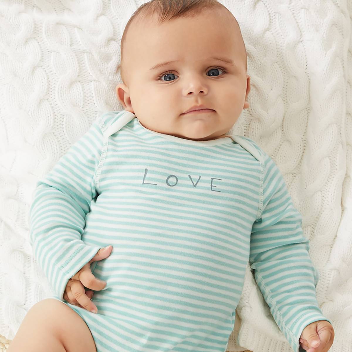 Baby wearing white and green striped babygrow. Shop babygrows
